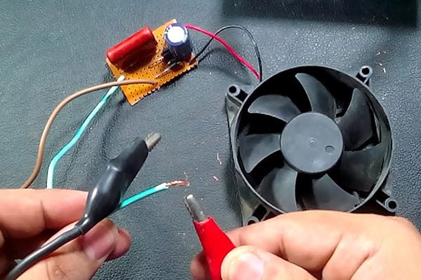 A multimeter's probes connected to the wires of a DC fan.