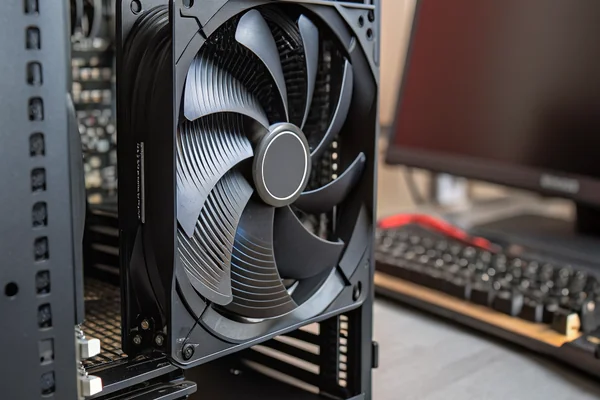 Close-up of a black 140mm PC case fan spinning, motion blur visible on the blades, mounted in an open computer case