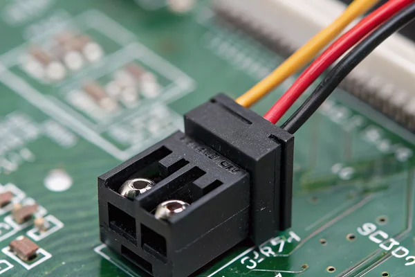 Close-up product photography of a small black 4-pin PWM fan connector, about the size of a fingertip, plugged onto a tiny matching pin header soldered on a green motherboard