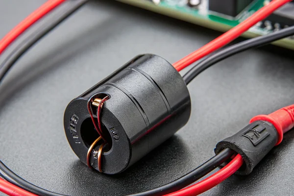 A black cylindrical snap-on ferrite bead clamped around the red and black power wires of a DC axial fan, clip-on toroid core for EMI suppression, macro product photography