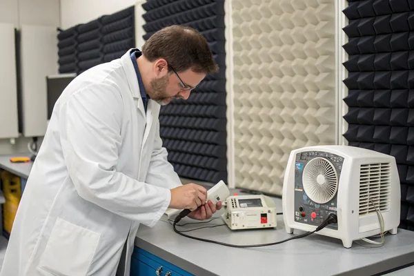 Engineer testing a small DC blower fan on a bench-top acoustic and pressure measurement setup in a quality lab
