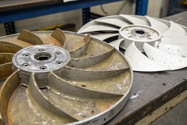 Close-up comparing metal spatter damage on a plastic fan blade against an undamaged metal fan blade