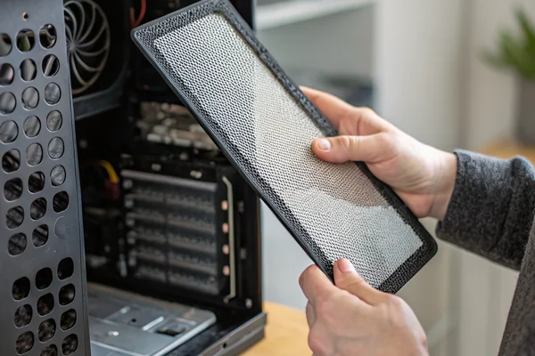 Close-up of a magnetic mesh intake filter being pulled off a black PC case front panel by hand, showing accumulated dust on the mesh surface