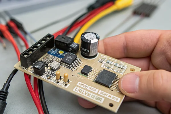 Close-up of a small PCB with a fan control IC and PWM circuitry, connected wire leads visible, held in a technician's hand
