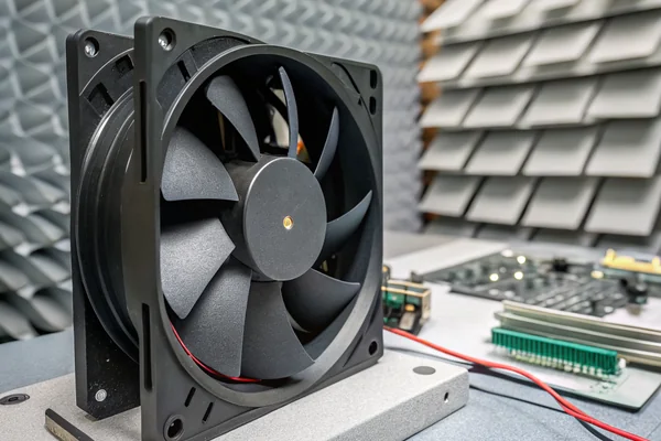 DC axial fan mounted inside a test fixture inside an anechoic chamber, with absorbent foam-covered walls visible in the background