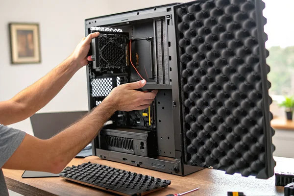 Person holding a PC case side panel lined with foam acoustic dampening material next to an open computer case