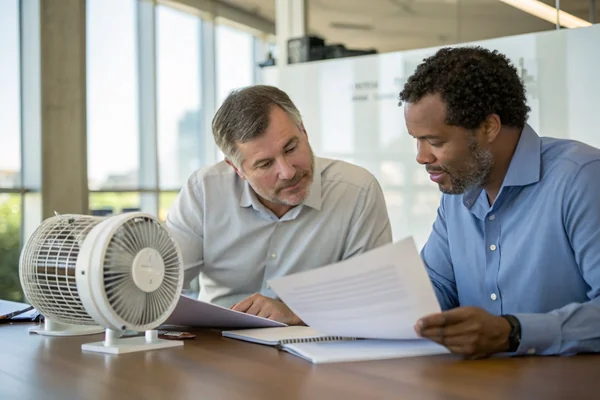 Engineer and manufacturer representative reviewing a printed fan specification document together at a conference table with a sample fan on the table