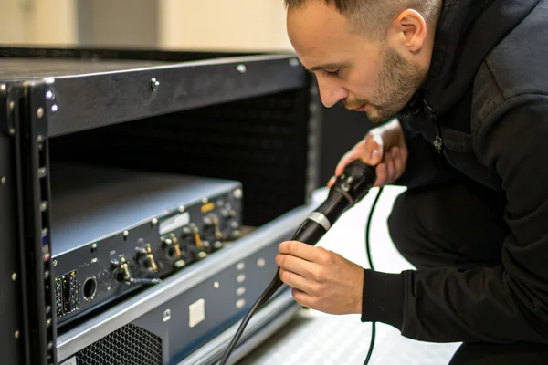 Technician using a contact microphone against the rear panel of a rack-mounted amplifier to locate vibration resonance from fan mounting