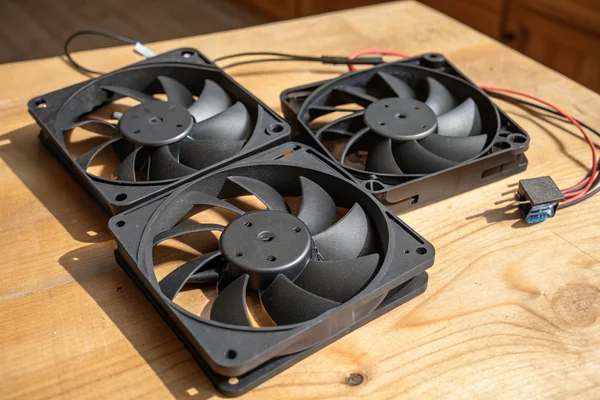 Three DC axial PC case fans with black frames laid flat on a workbench, showing blade and hub detail