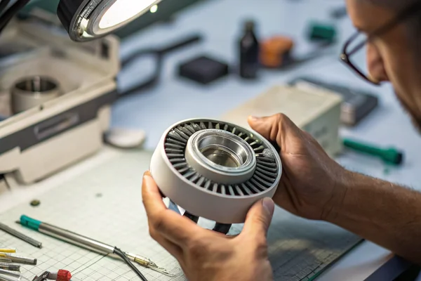 Technician inspecting a failed DC axial fan's bearing assembly under magnification at an analysis workbench