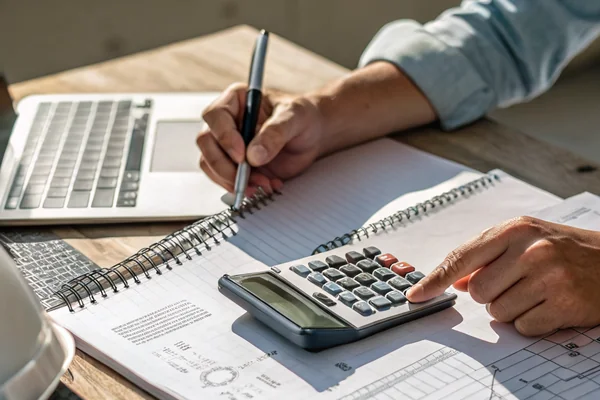 Engineer using a calculator and reference chart to work through a fan airflow sizing calculation at a desk
