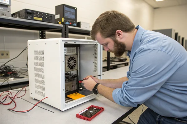 Engineer testing a small case fan's performance inside a compact enclosure mockup on a lab bench