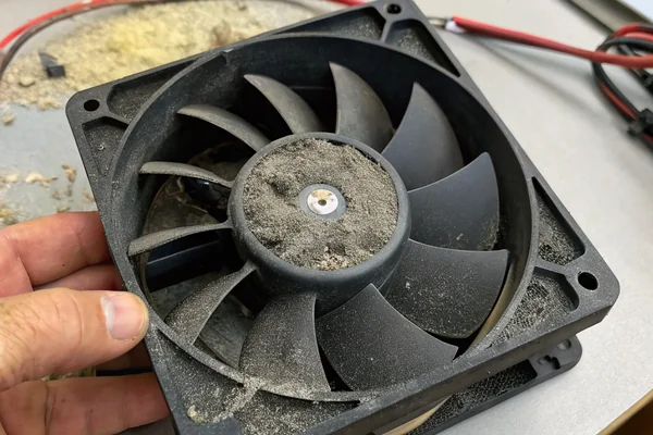 Close-up of a dust-clogged DC axial fan removed from equipment, thick gray lint accumulation visible on the blades and hub