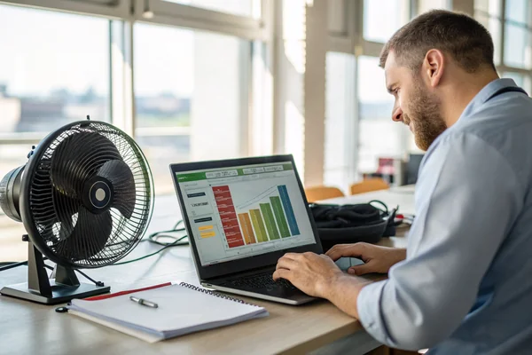 Engineer reviewing an energy consumption chart on a laptop screen next to a cooling fan on a workbench