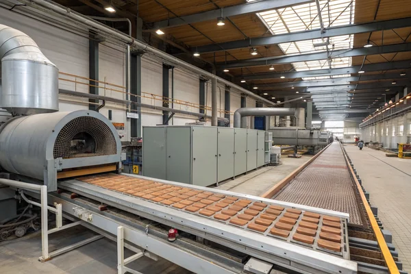 Wide shot of an industrial drying oven production line with material passing through on a conveyor, ductwork and blower equipment visible along the side
