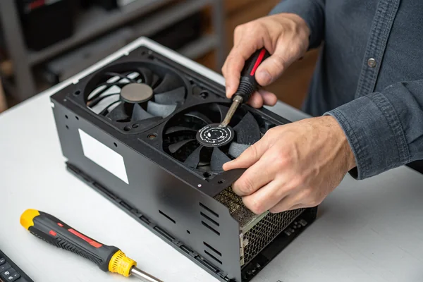 Hands installing a new black PC case fan into a mid-tower case mounting bracket with a screwdriver nearby