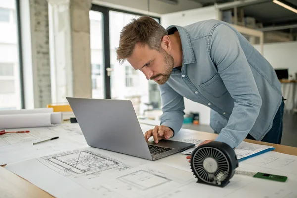 Engineer reviewing laptop chassis design drawings alongside a sample thin blower fan on a design desk