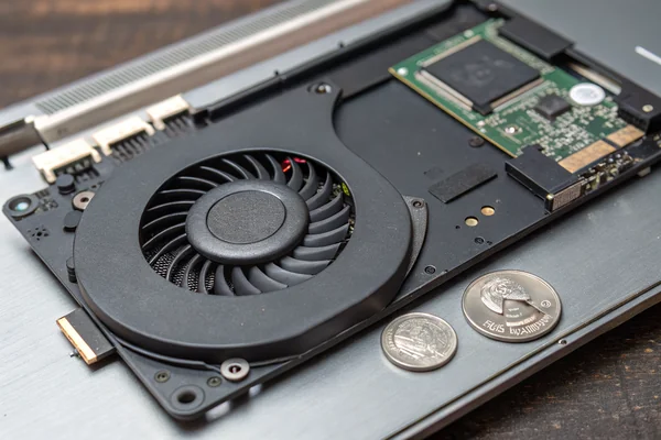 Extremely thin DC blower fan removed from an ultra-thin laptop, showing its low-profile centrifugal design next to a coin for scale